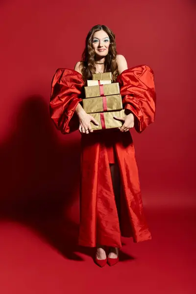 A vibrant young woman in an elegant red gown joyfully presents wrapped gifts. — Stock Photo