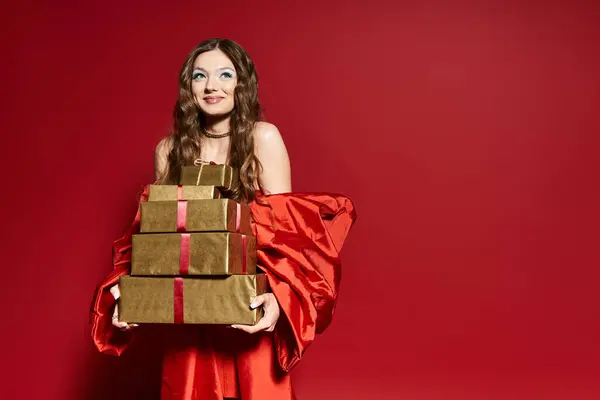 A vibrant young woman dressed in a red outfit smiles while holding elegantly wrapped gifts. — Stock Photo