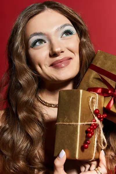 A cheerful young woman with wavy hair smiles while holding golden, ribbon adorned gifts. — Stock Photo
