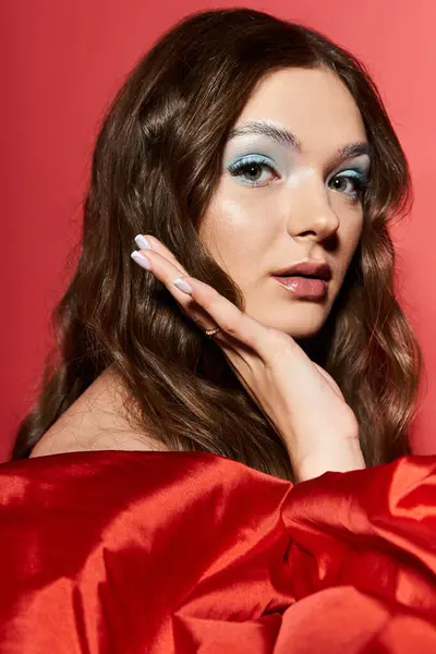 Una giovane donna elegante con i capelli lunghi mette in mostra la sua bellezza su uno sfondo rosso sorprendente. — Foto stock