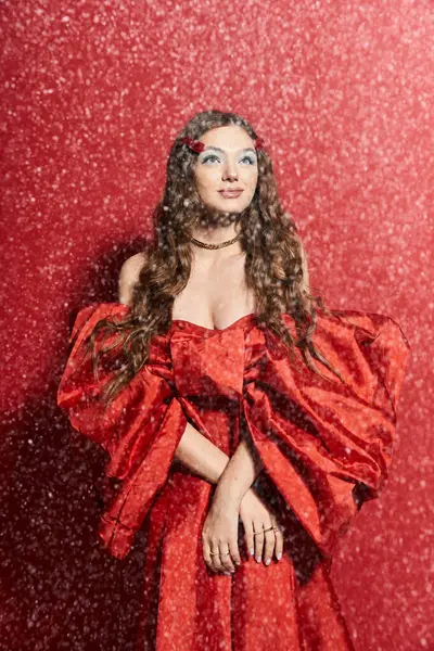 The young woman stands elegantly, adorned in a striking red gown, exuding confidence and charm. — Stock Photo