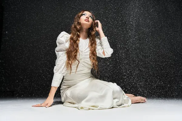 A graceful young woman in a stunning white dress interacts with the swirling glittering light. — Stock Photo