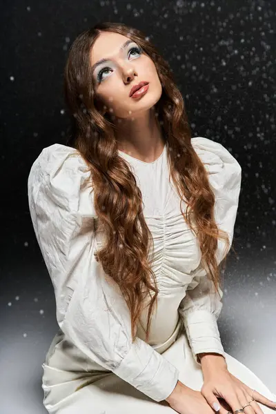 A beautiful young woman with flowing hair gazes upwards as delicate snowflakes fall around her. — Stock Photo
