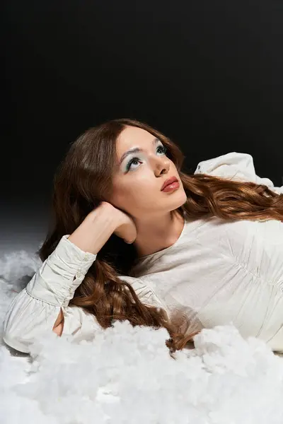 The young woman lies gracefully on fluffy clouds, lost in thought under soft lighting. — Stock Photo