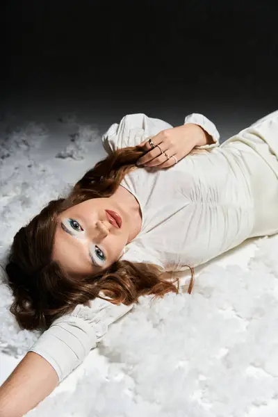 A stunning young woman lies on a soft white surface, exuding elegance and tranquility. — Stock Photo