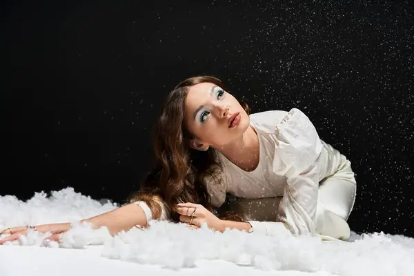 Uma jovem encontra-se entre a neve fofa, olhando para cima pensativo como flocos de neve vagando suavemente em torno dela. — Fotografia de Stock