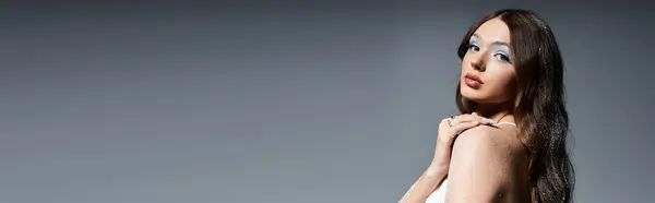 A stunning young woman showcases her elegance while gently touching her shoulder in soft light. — Stock Photo