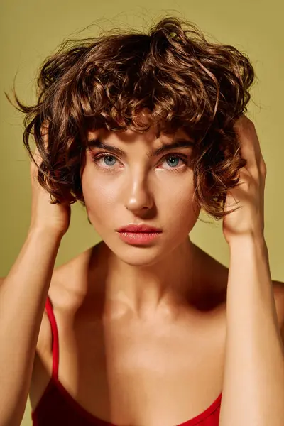 A young woman with curly hair holds her head, conveying strong emotions in a gentle setting. — Stock Photo
