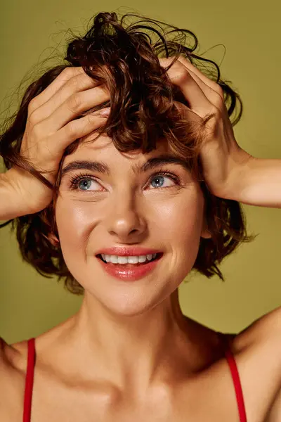 A young woman joyfully smiles while holding her curly hair, radiating happiness and warmth. — Stock Photo