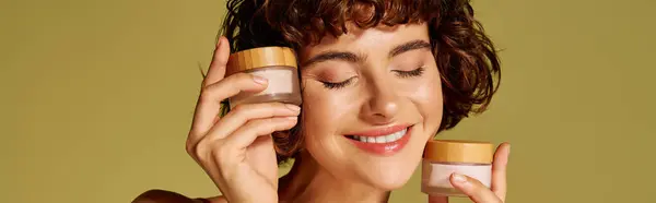 A young woman beams with happiness while holding skincare containers. — Stock Photo