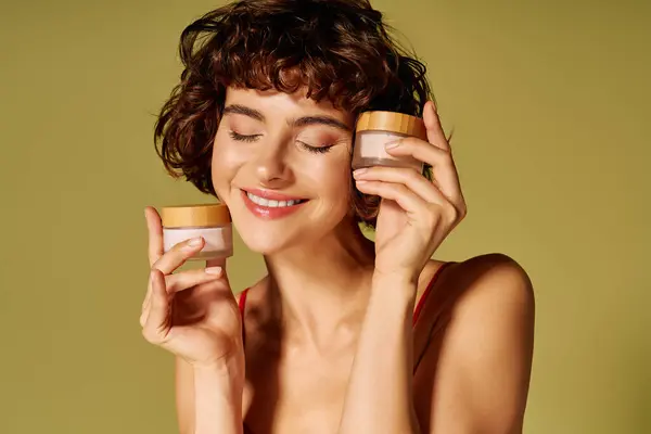 A cheerful young woman embraces skincare jars with a joyful smile, radiating happiness. — Stock Photo