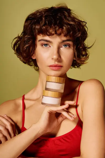 The woman showcases skincare jars while expressing a deep emotional response in a creative space. — Stock Photo
