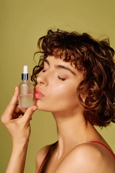 A woman delicately holds a skincare serum against her cheek, radiating happiness and self care. — Stock Photo