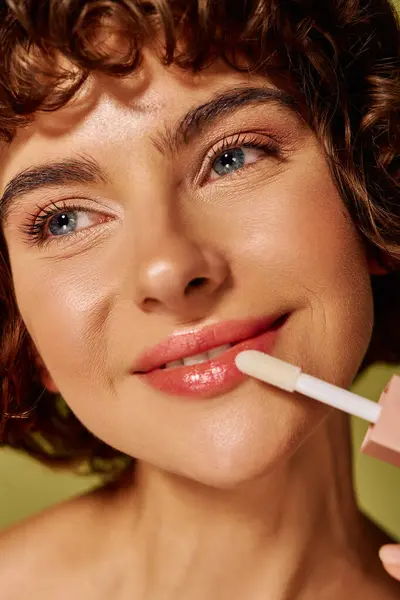 The young woman joyfully enhances her lips with gloss, radiating happiness and warmth. — Stock Photo