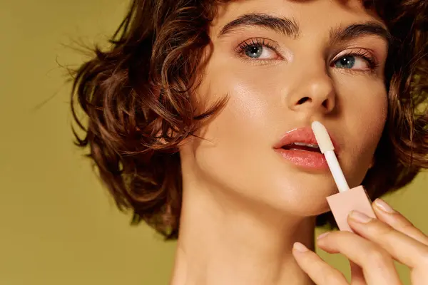 The young woman gently applies lip gloss while lost in deep thought, showcasing her emotions. — Stock Photo