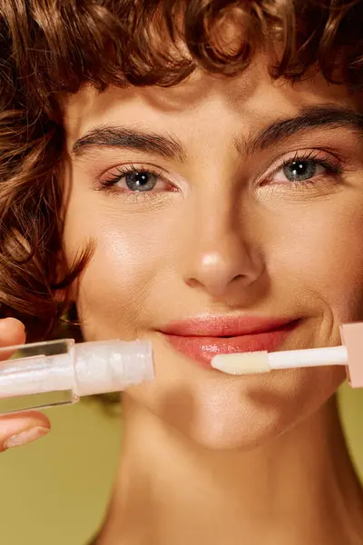 A young woman smiles brightly as she applies lip gloss, radiating happiness and confidence. — Stock Photo