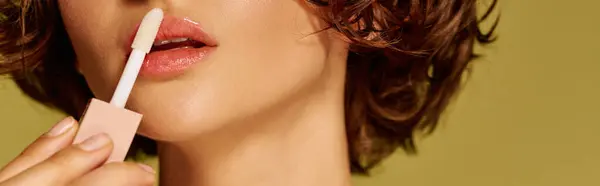 A young woman applies lip gloss, her emotional expression contrasting a colorful backdrop. — Stock Photo