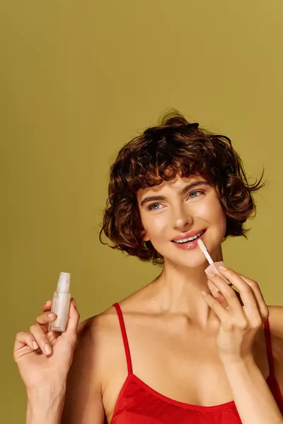 The young woman beams with joy as she applies a glossy lip product, showcasing her radiant beauty. — Stock Photo