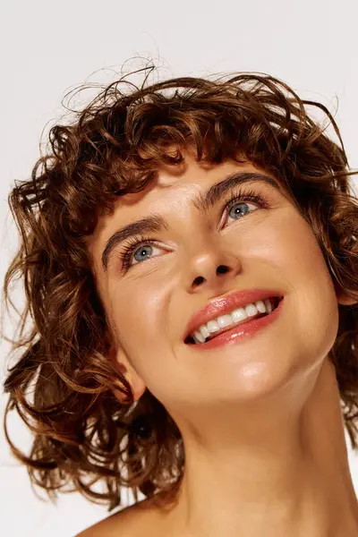 A young woman with curly hair beams with happiness, looking skyward in bright surroundings. — Stock Photo