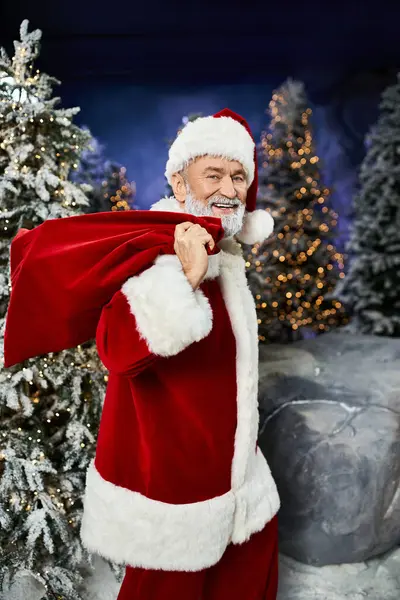 A smiling Santa holds a big sack of gifts, surrounded by snow. — Stock Photo