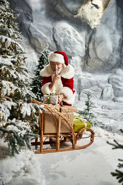 Santa Claus quietly organizes wrapped presents while surrounded by a magical winter landscape. — Stock Photo