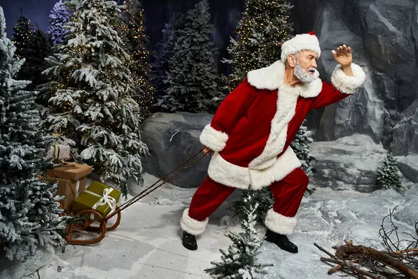 A joyful Santa Claus navigates through a snowy forest while pulling a sled full of presents. — Stock Photo