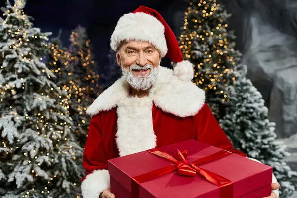 Papai Noel alegremente oferece um presente embrulhado em uma floresta nevada e festiva. — Fotografia de Stock