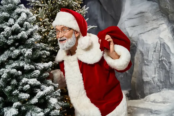 A joyful figure dressed as Santa Claus prepares gifts while standing near snow covered trees. — Stock Photo