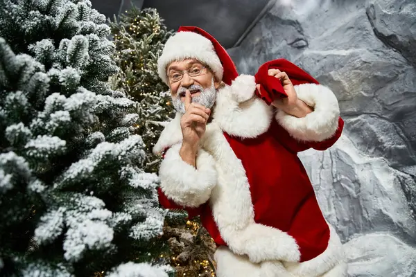 An energetic figure in a red costume playfully signals for silence among decorated trees. — Stock Photo