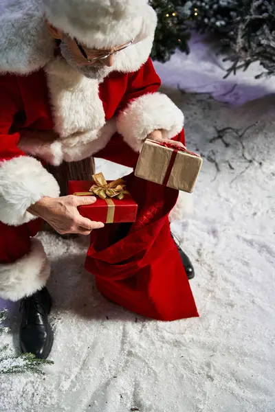 A jolly figure in a red suit thoughtfully selects presents from a festive sack. — Stock Photo