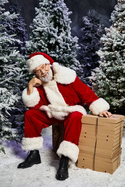 A joyful Santa Claus sits beside stacked presents, surrounded by a winter wonderland of snow. — Stock Photo