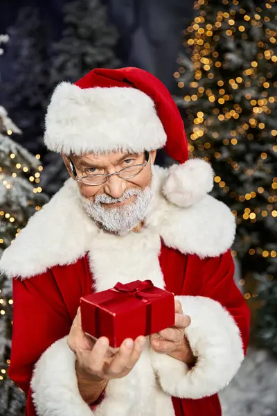 A cheerful figure in a red suit holds a small gift, surrounded by a winter wonderland atmosphere. — Stock Photo