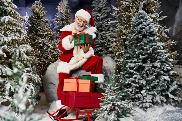 Santa Claus is happily arranging colorful presents in a snowy forest setting filled with trees. — Stock Photo
