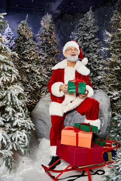 A cheerful figure in red and white attire holds gifts, surrounded by snow dusted trees. — Stock Photo