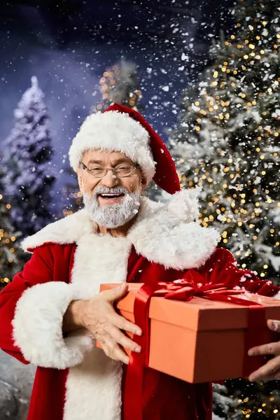 A joyful Santa holds a wrapped gift in a snowy scene. — Stock Photo