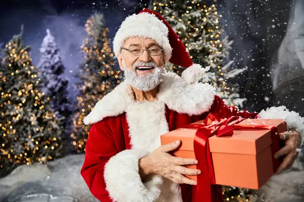 Une silhouette joyeuse habillée comme le Père Noël propage la joie des fêtes tout en tenant un cadeau au milieu des chutes de neige. — Photo de stock