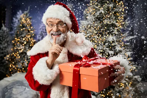 A joyful figure dressed as Santa Claus holds a beautifully wrapped gift and smiles warmly. — Stock Photo