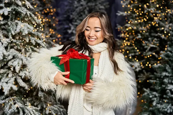 A young woman joyfully holds a beautifully wrapped Christmas gift in a festive setting. — Stock Photo