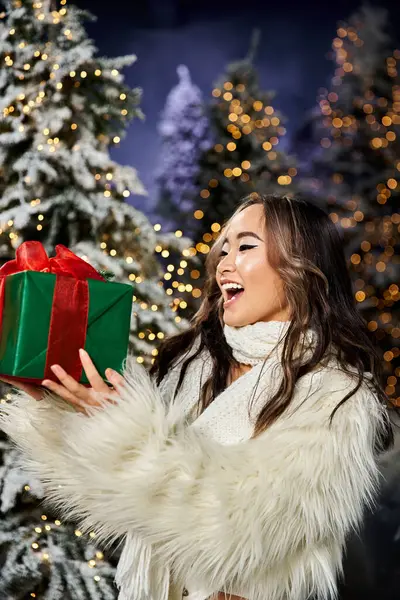 A woman delights in receiving a festive gift amidst twinkling lights and snow covered trees. — Stock Photo