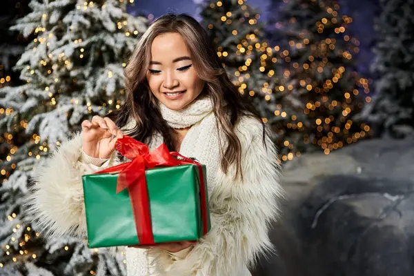 Eine entzückte junge Frau enthüllt ein wunderschön verpacktes Weihnachtsgeschenk vor verschneiter Kulisse. — Stockfoto