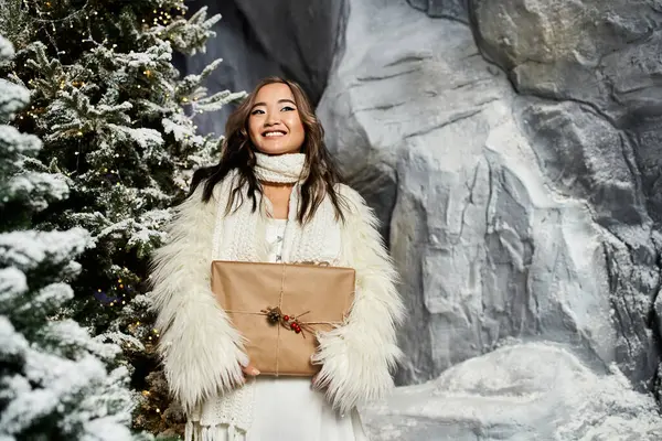 A woman smiles brightly with a wrapped gift in a magical Christmas scene. — Stock Photo