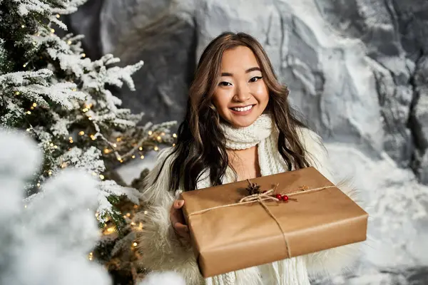 A woman smiles brightly while holding a wrapped present amid a charming Christmas backdrop. — Stock Photo