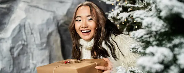 A cheerful woman in a cozy outfit smiles while revealing a surprise gift in a snowy setting. — Stock Photo