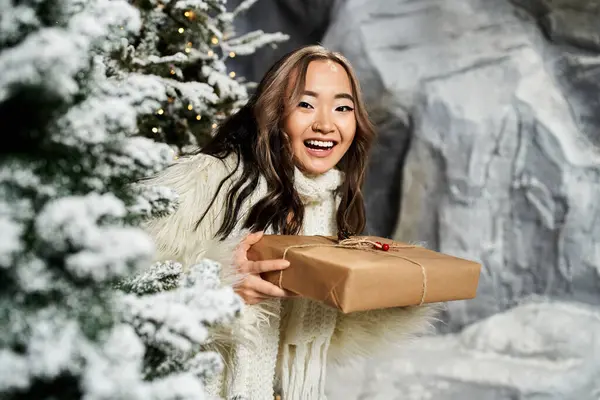 A cheerful young woman holds a beautifully wrapped gift while surrounded by festive holiday decor. — Stock Photo