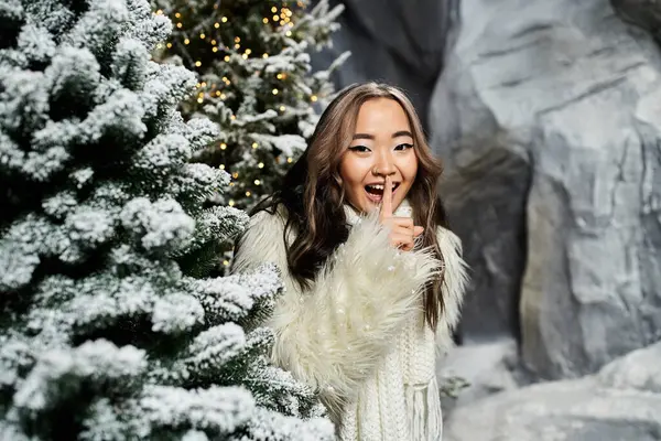 A joyful individual playfully gestures for silence surrounded by snowy Christmas trees. — Stock Photo