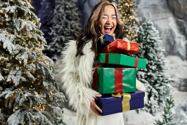 Uma pessoa alegre no desgaste do inverno carrega presentes de Natal coloridos entre a decoração do feriado. — Fotografia de Stock