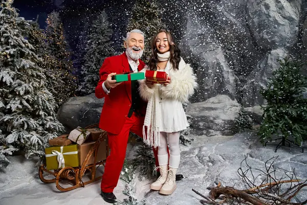 A cheerful duo holds brightly wrapped presents while surrounded by a winter wonderland. — Stock Photo