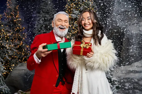 A cheerful moment unfolds as two people share festive gifts against a snowy Christmas backdrop. — Stock Photo