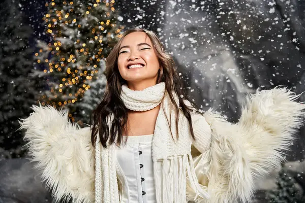 Una joven disfruta alegremente de la atmósfera nevada, rodeada de luces y árboles centelleantes. - foto de stock