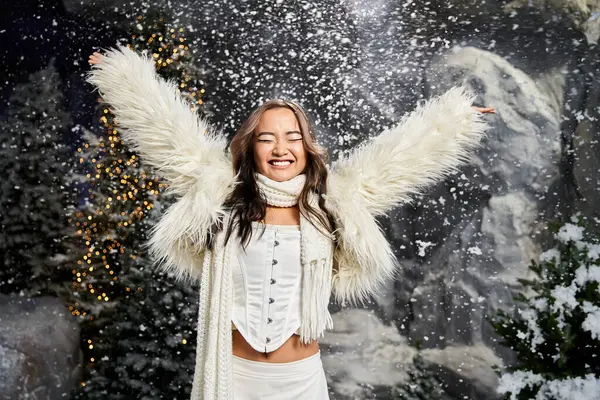 Una donna in un cappotto bianco soffice abbraccia gioiosamente l'inverno mentre i fiocchi di neve cadono intorno a lei. — Foto stock